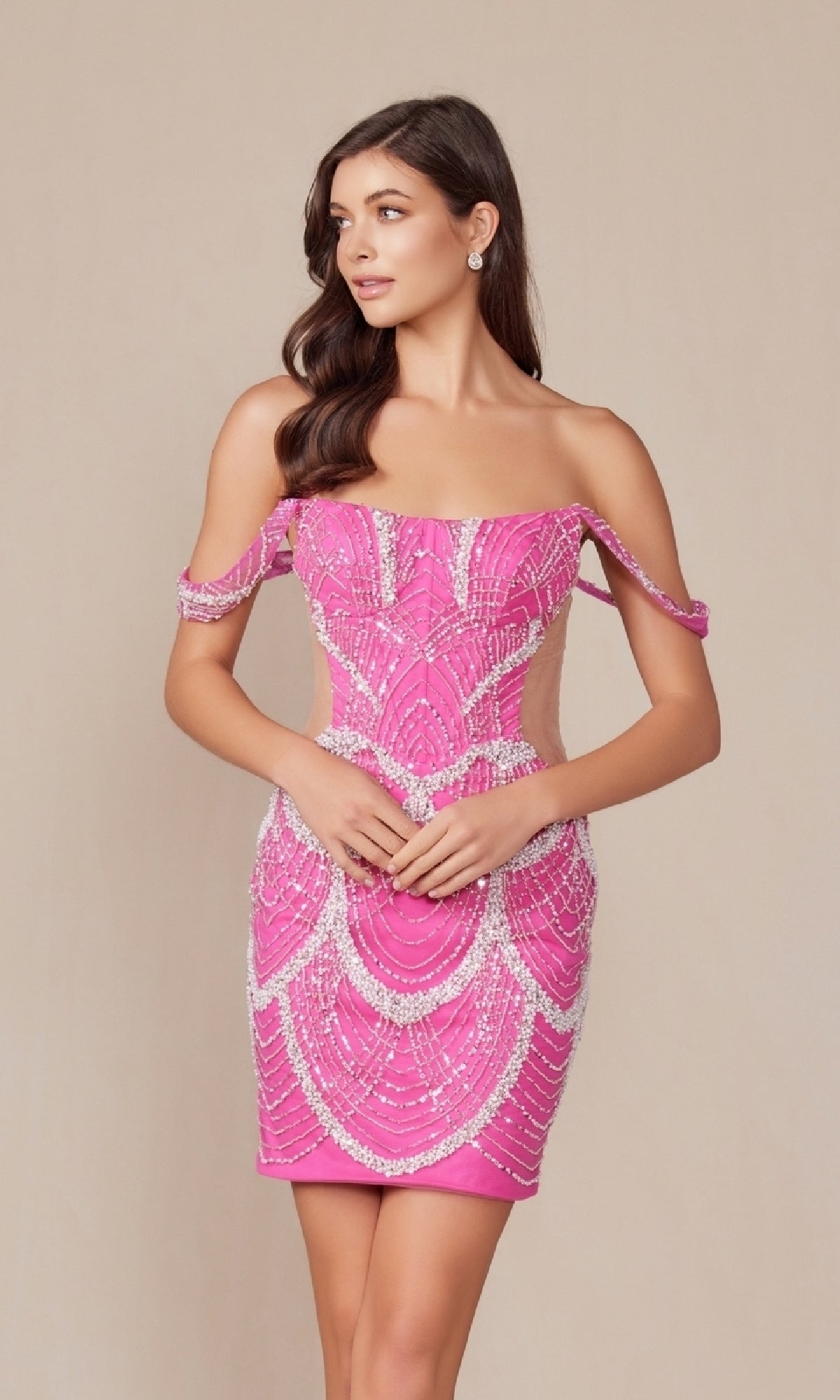 A woman models the Sheer-Sides Short Sexy Homecoming Dress Q839, a fitted pink off-the-shoulder dress with intricate beadwork, standing gracefully against a plain beige background.